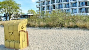 A modern multi-story hotel with a flat roof and balconies, situated on a sandy beach with sparse vegetation. - SeeHuus Lifestyle Hotel (Timmendorfer Strand)