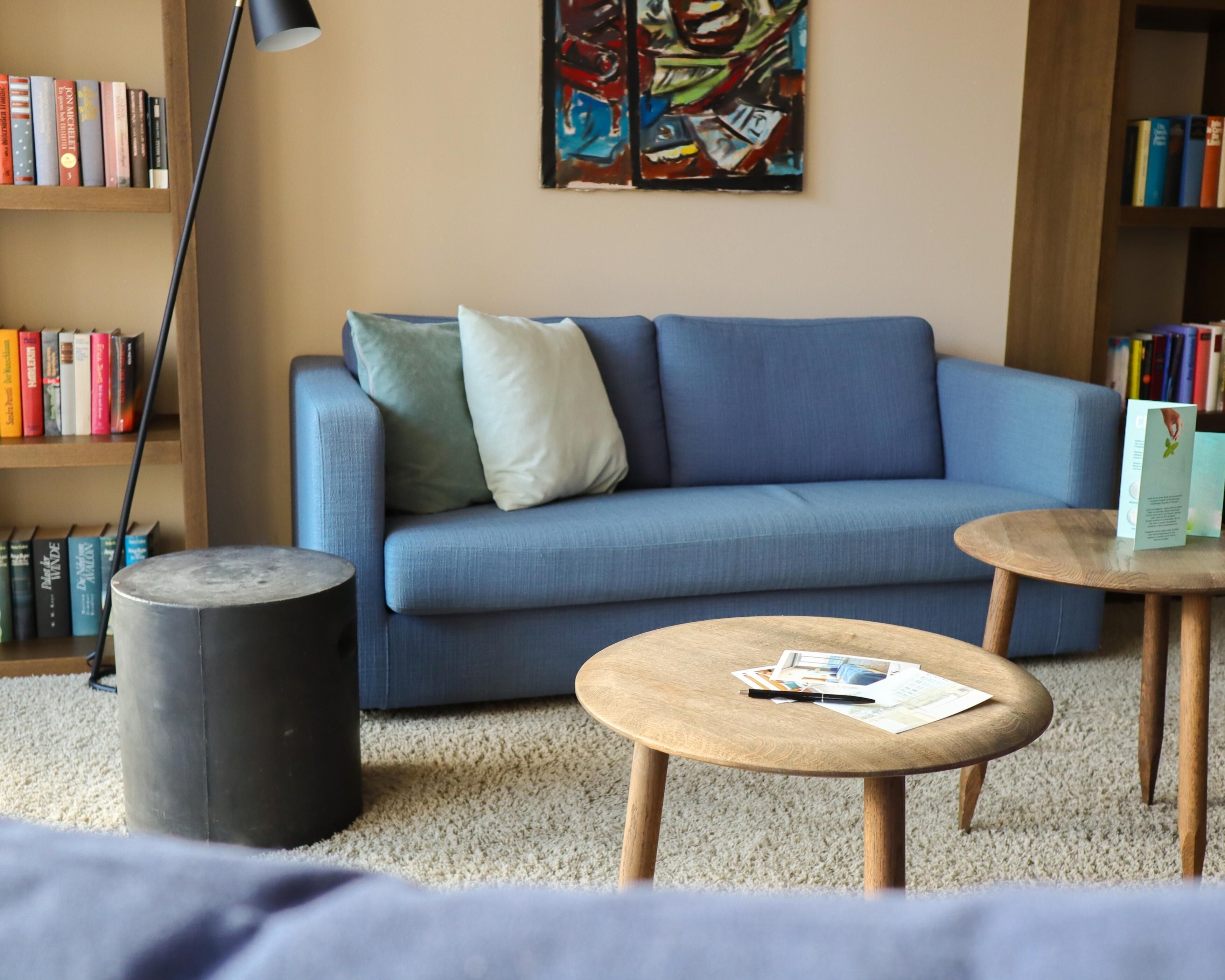 A modern living room with a blue sofa, a round wooden coffee table, a black floor lamp, and a bookshelf filled with books.
