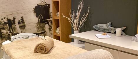A spa room with a massage table, towels, a decorative plant, and a vintage photo on the wall.
