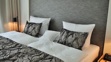 A neatly made bed with white linens and black patterned pillows, a grey headboard, and a bedside table with a phone.