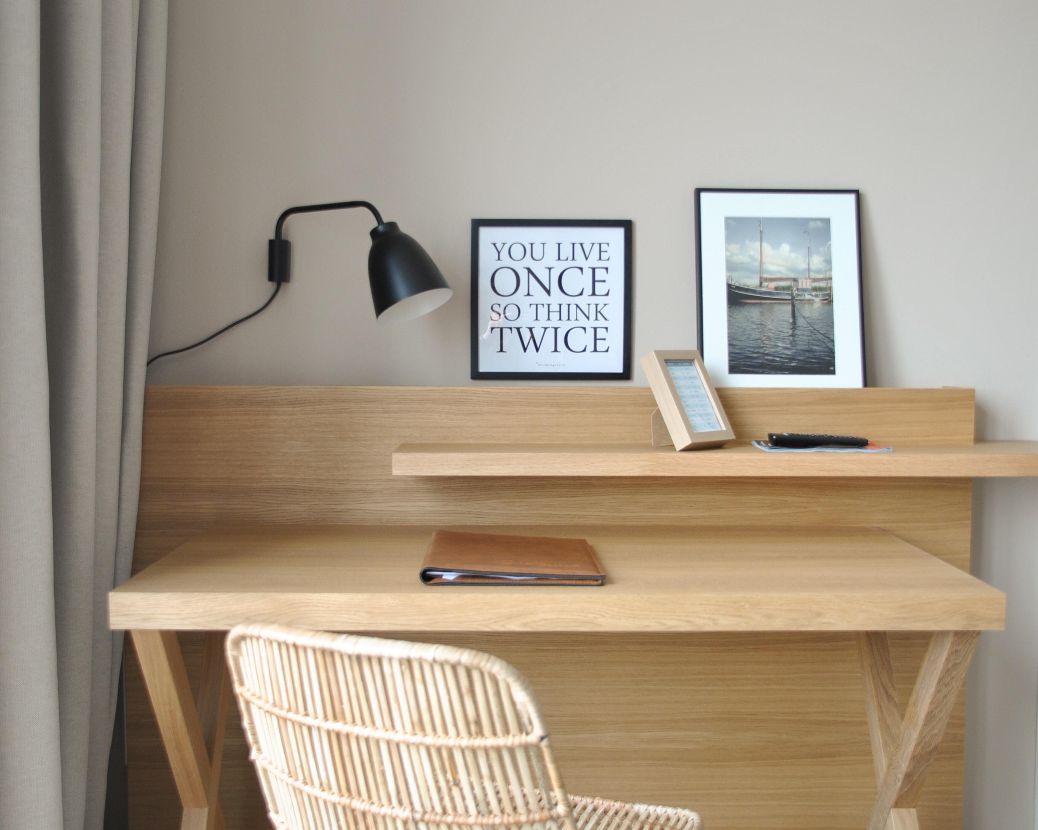 A wooden desk with a laptop, a framed quote, a picture frame, and a lamp.
