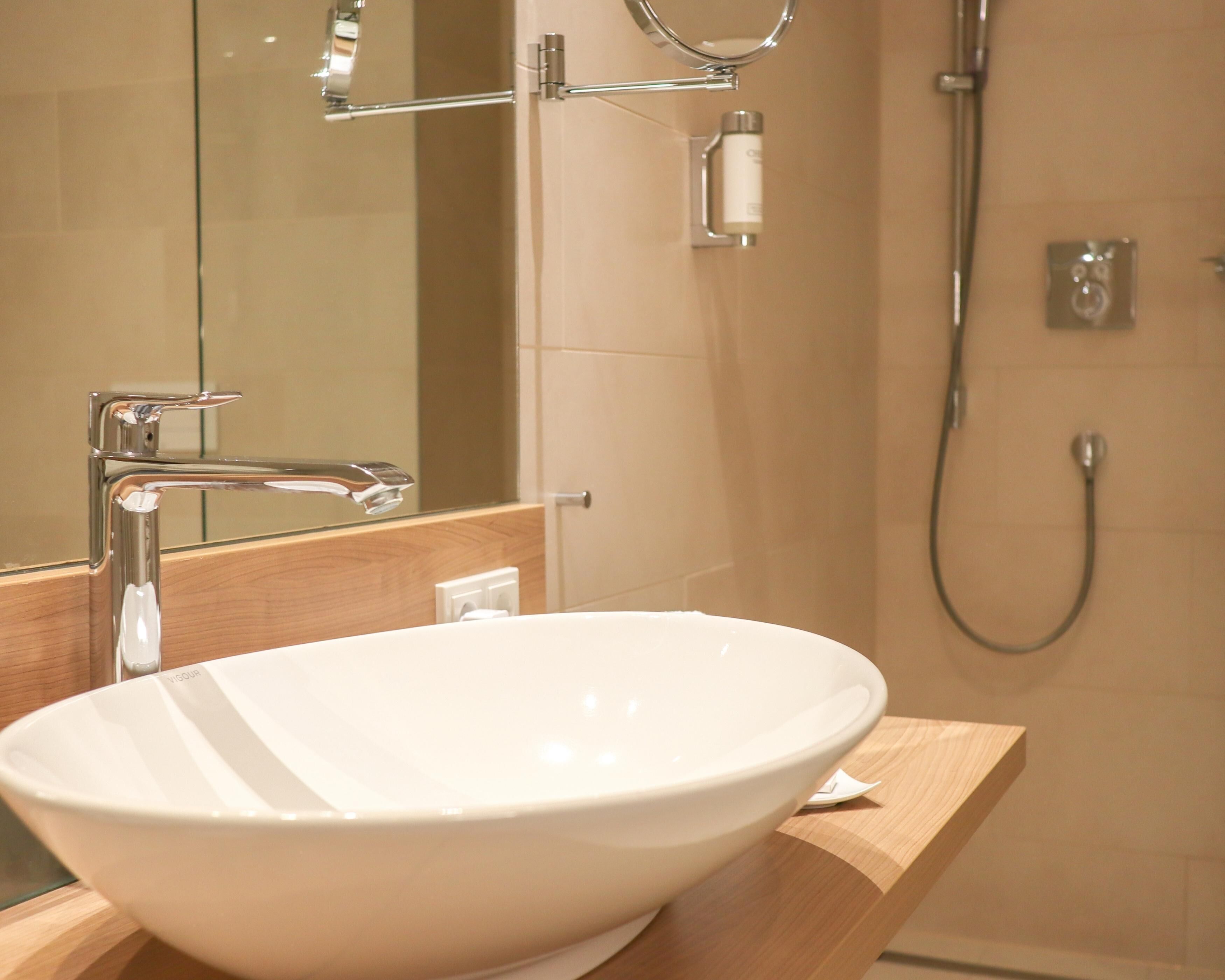 Une salle de bain avec un lavabo sur colonne blanc, un miroir, une douchette à main et un distributeur de serviettes.