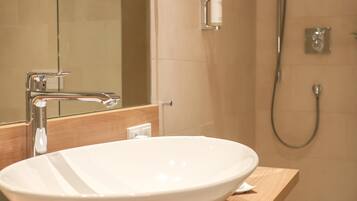 Une salle de bain avec un lavabo sur colonne blanc, un miroir, une douchette à main et un distributeur de serviettes.