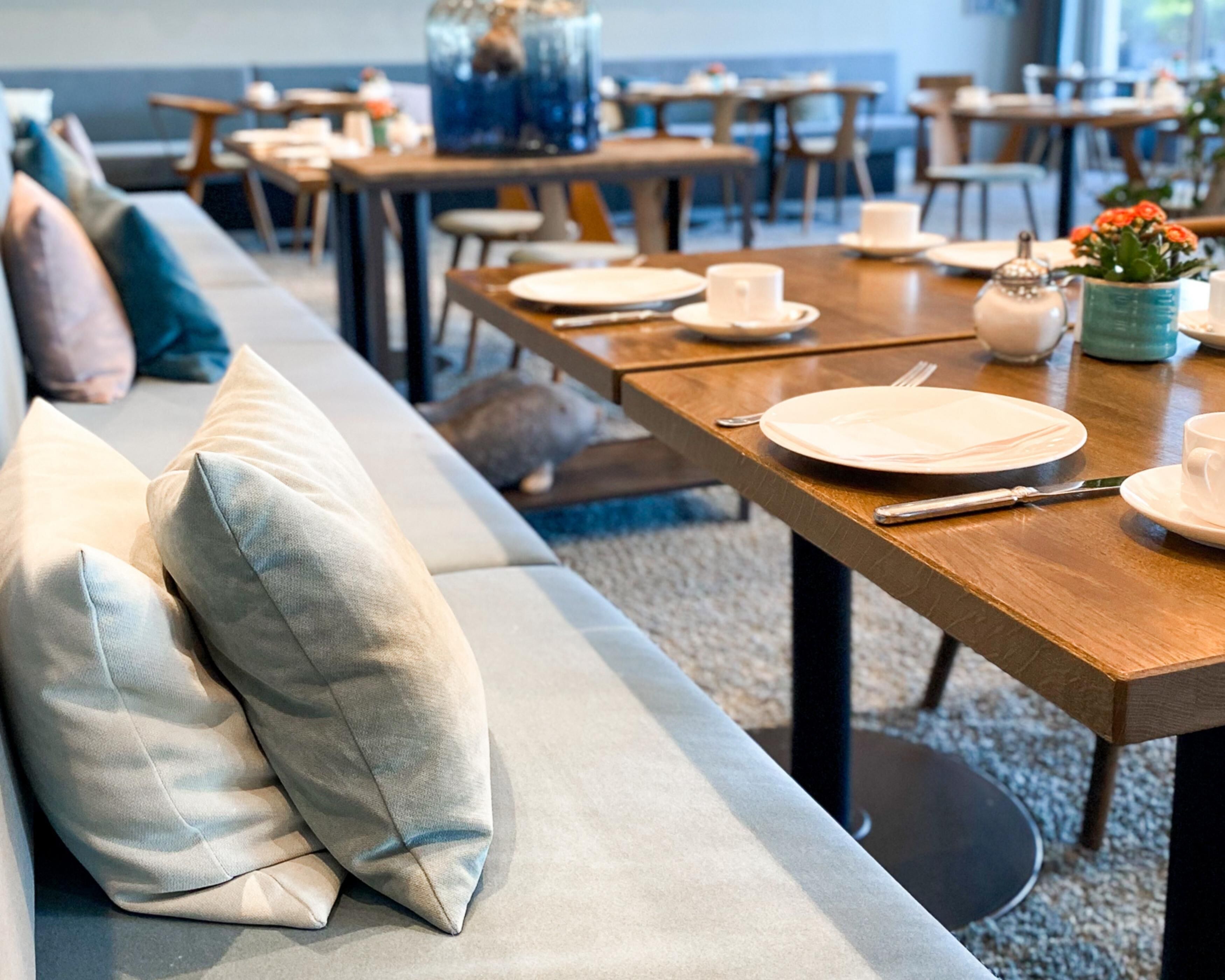 A dining area with tables set for service, a sofa with cushions, and a decorative vase.
