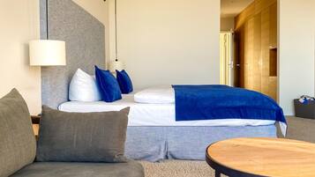 A modern hotel room with a bed, a sofa, a round wooden table, and a wardrobe.