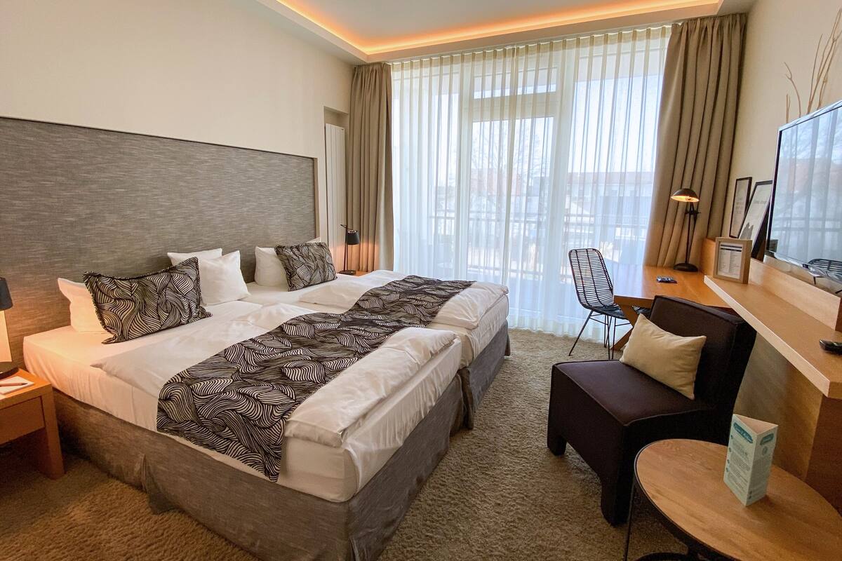 Ein Hotelzimmer mit einem großen Bett, einem Schreibtisch, einem Sessel und einem Fernseher.