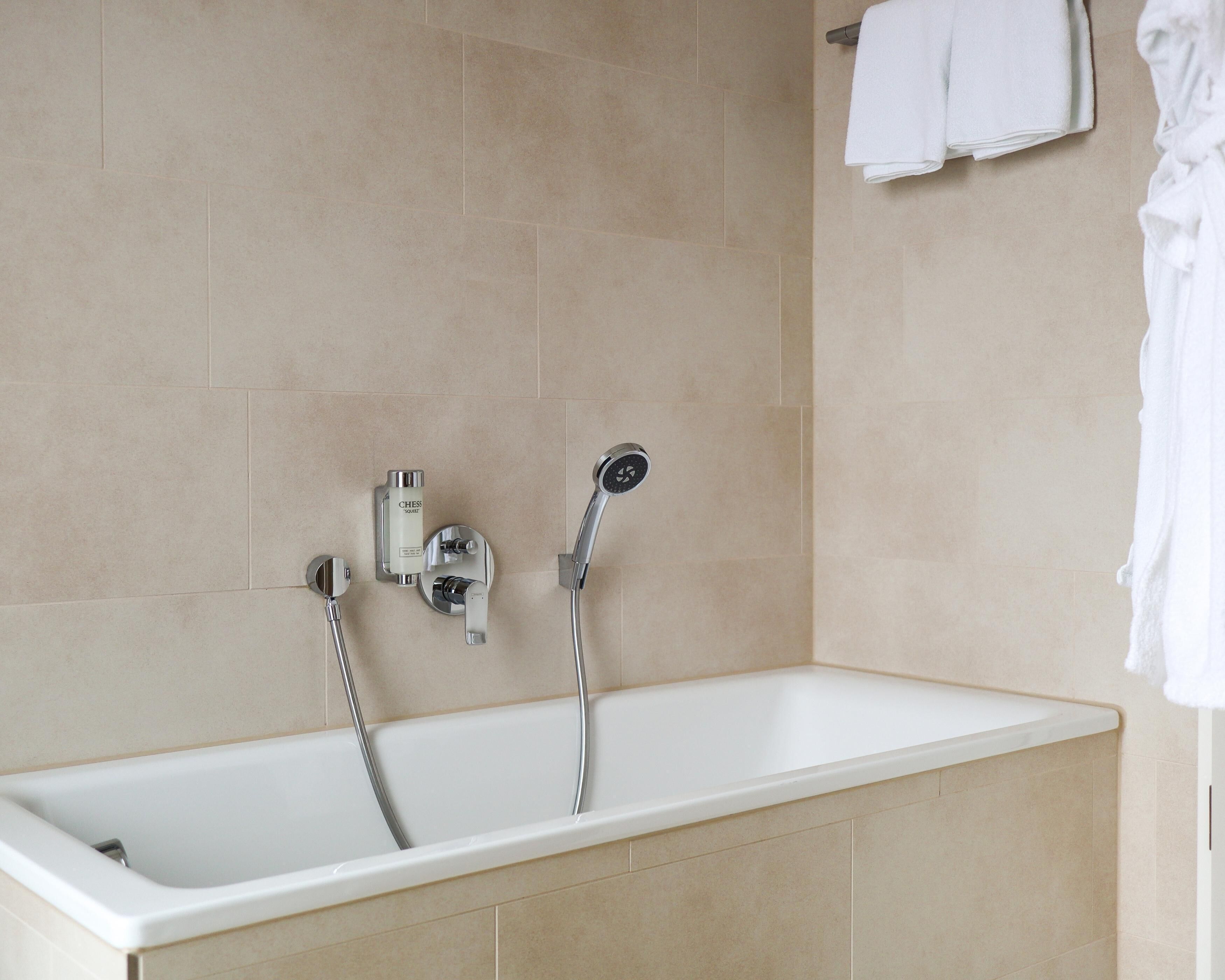 A modern bathroom with a bathtub, a handheld showerhead, and a wall-mounted faucet.