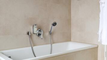 A modern bathroom with a bathtub, a handheld showerhead, and a wall-mounted faucet.