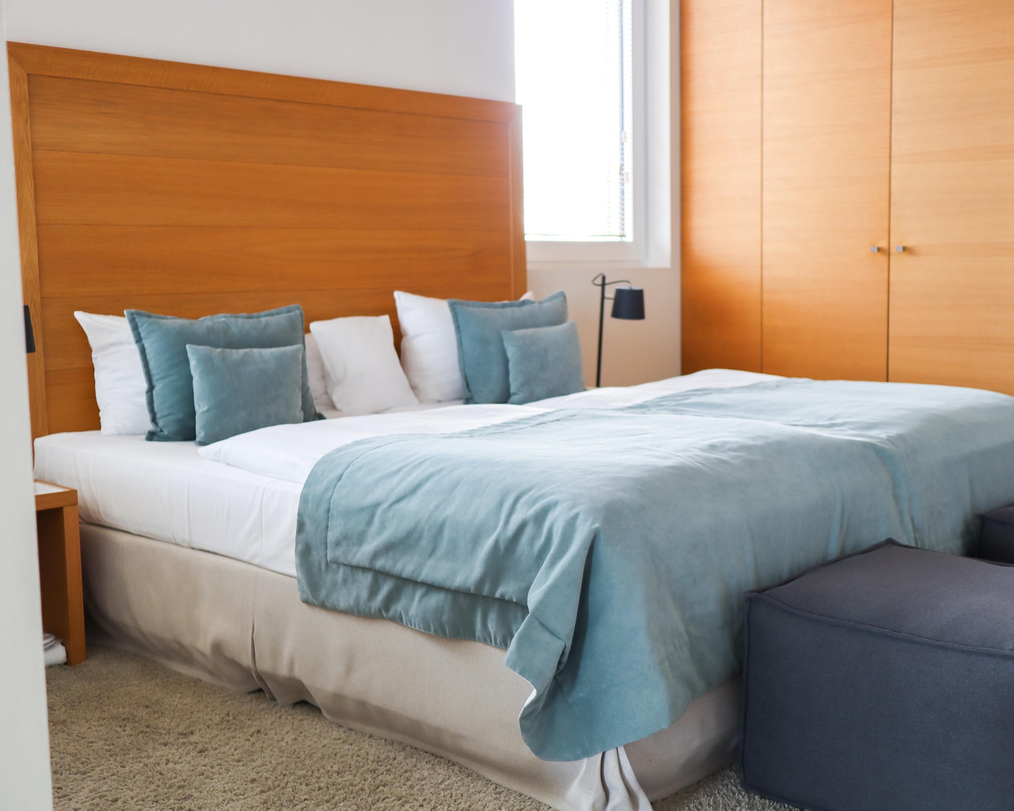 Un dormitorio con cabecera de madera, cama con ropa de cama blanca y azul, una lámpara de noche y un armario.
