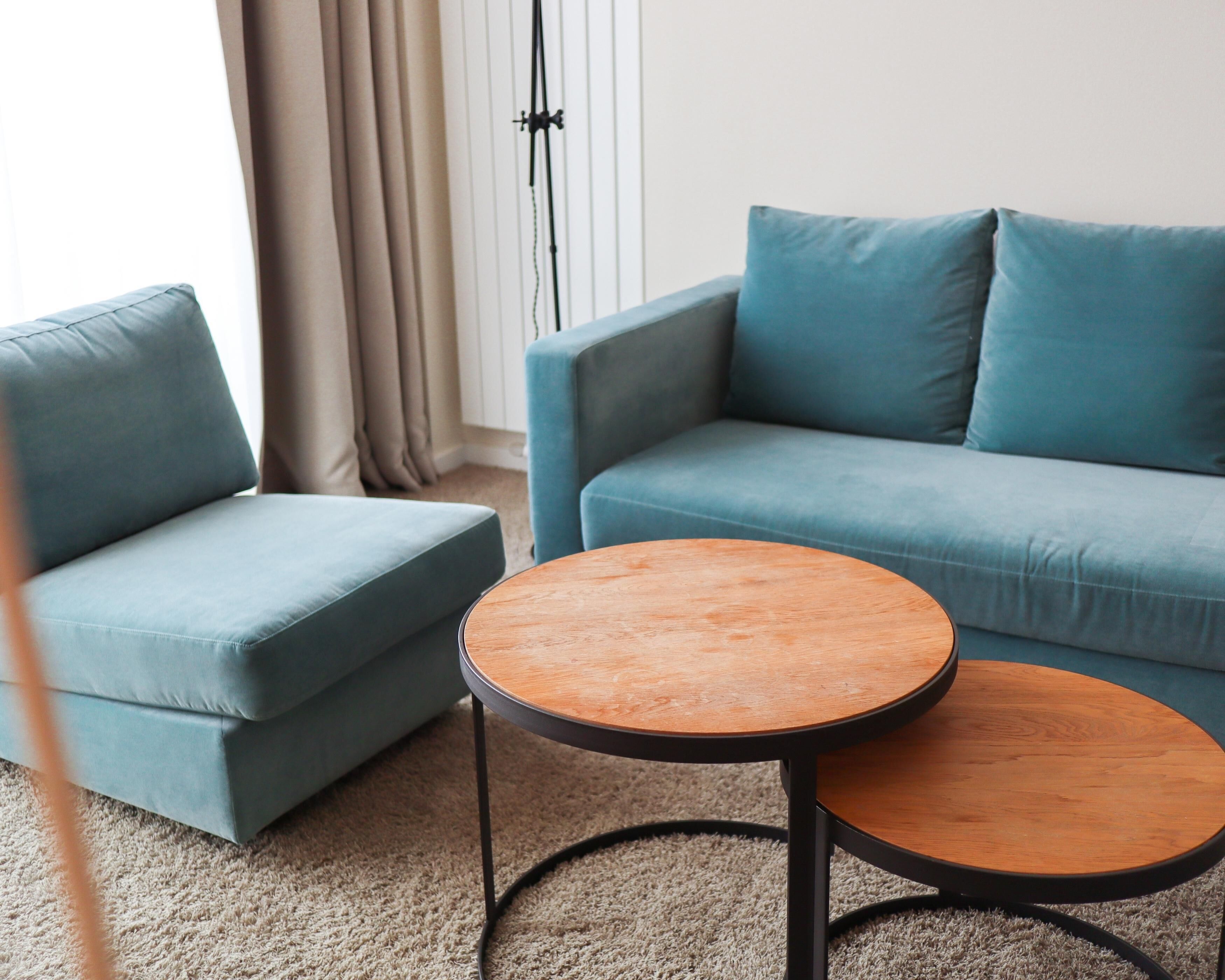 A living room with a blue sofa, a matching armchair, and two round wooden tables.