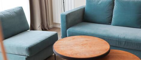 A living room with a blue sofa, a matching armchair, and two round wooden tables.