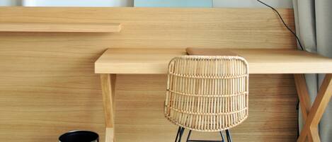 A wooden desk with a woven chair, a wall-mounted lamp, and a motivational quote poster.