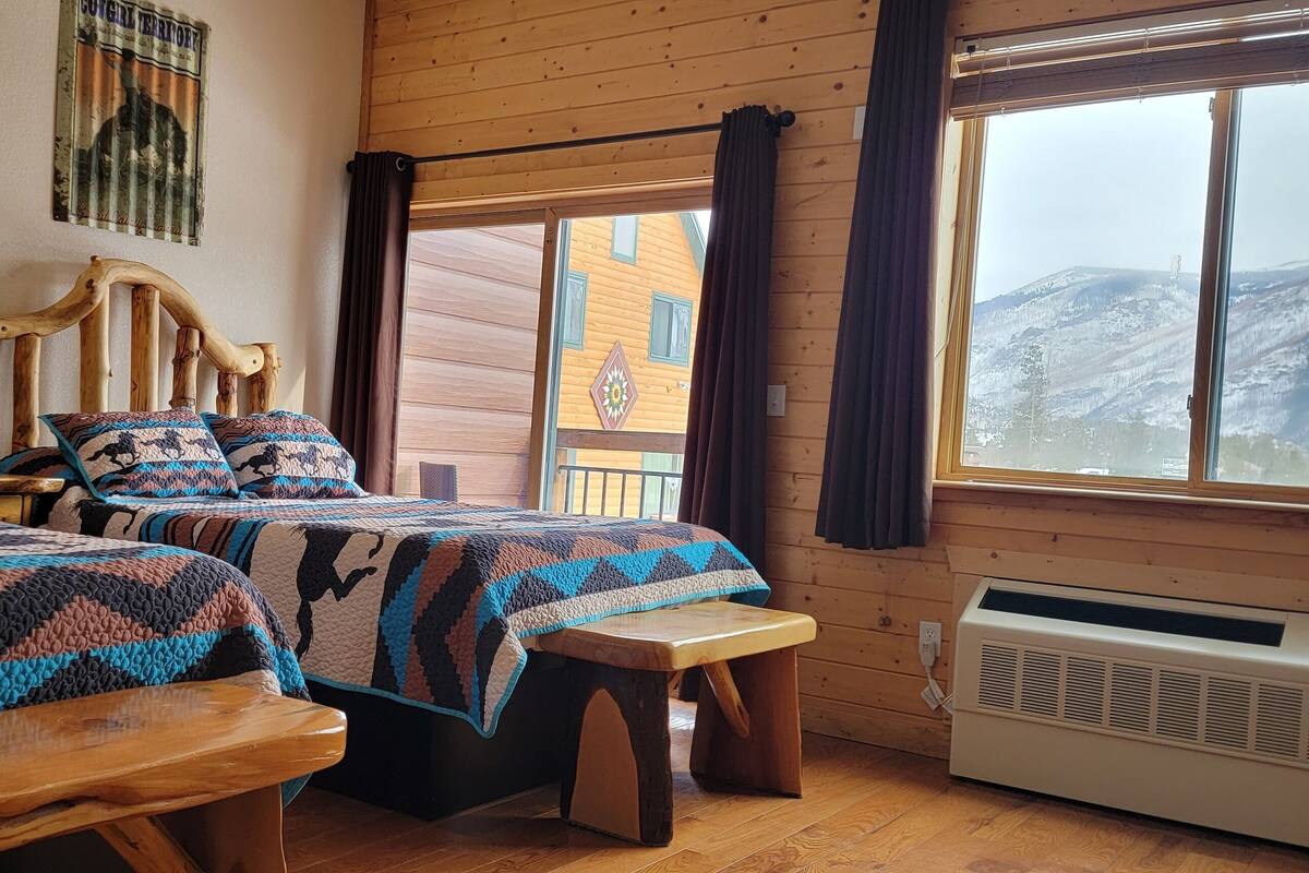 A cozy room with two wooden beds, a bench, and a large window with a view of a mountain.