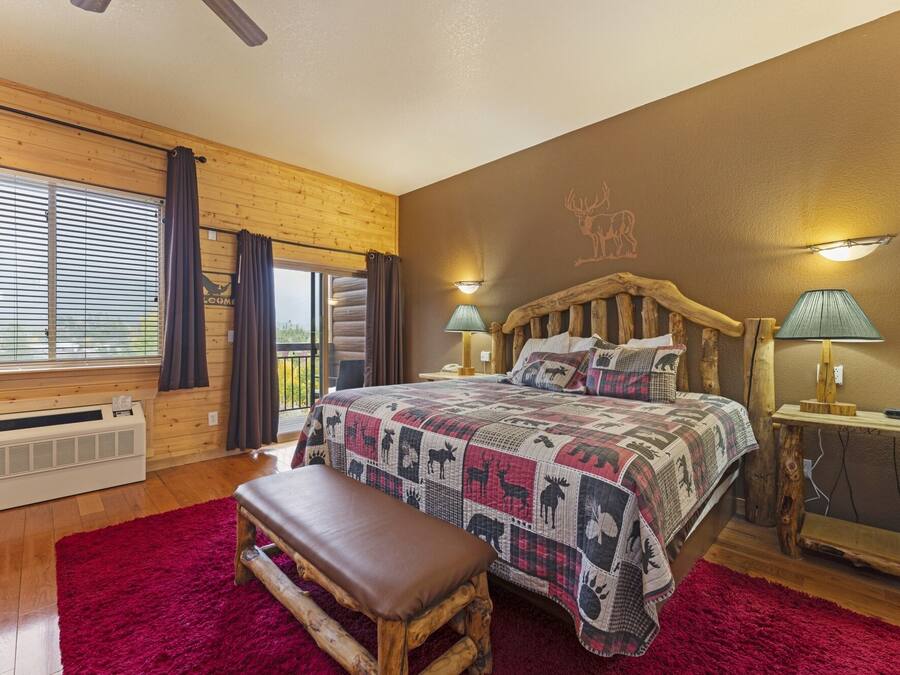Une pièce chaleureuse avec une tête de lit en bois, un grand lit recouvert d’une courtepointe à motifs, un banc et un tapis rouge.