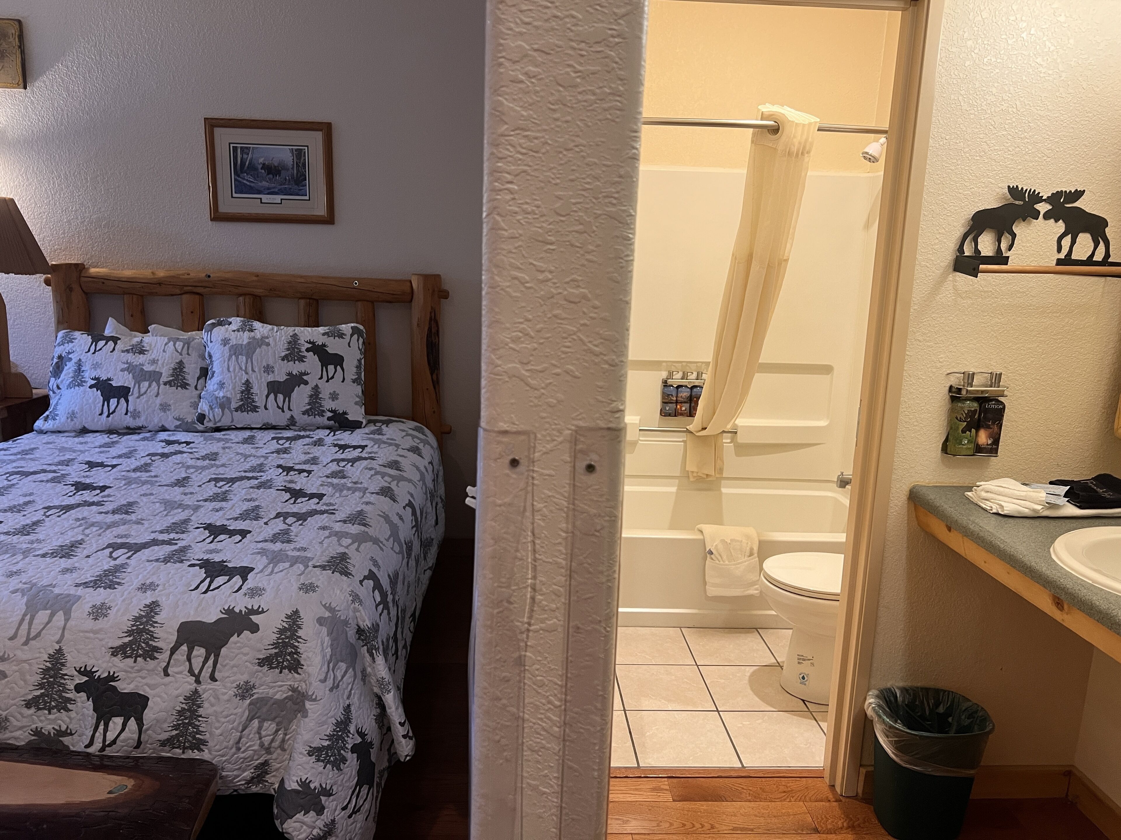 Quarto com cama, edredom e almofadas com tema de alce, cabeceira de madeira e um quadro na parede.