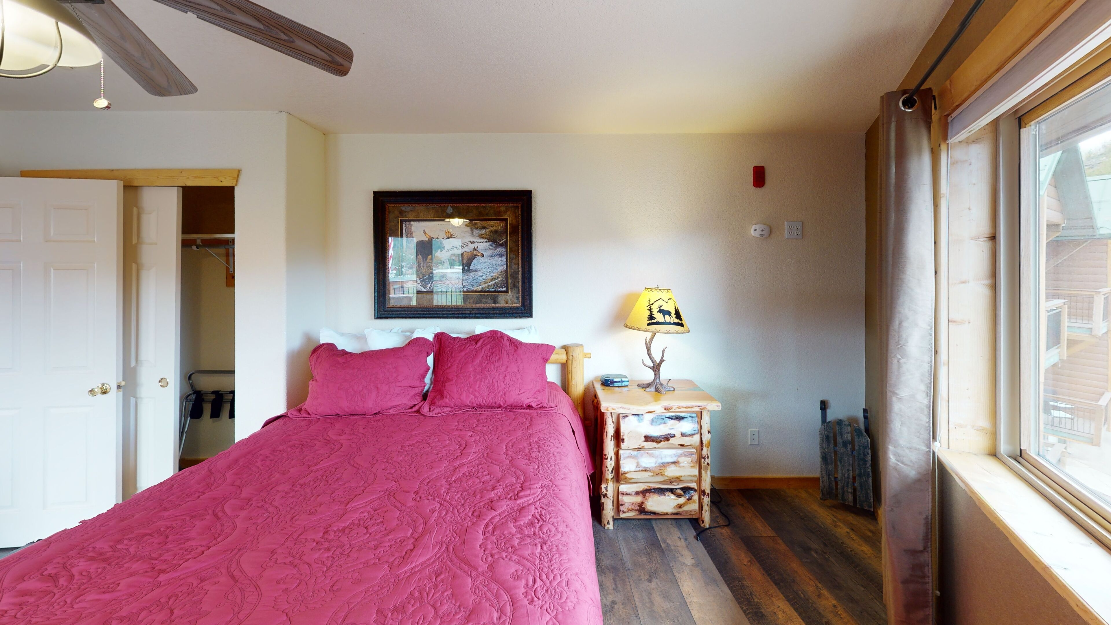 A bedroom with a bed, a nightstand, a lamp, a framed picture, and a window.
