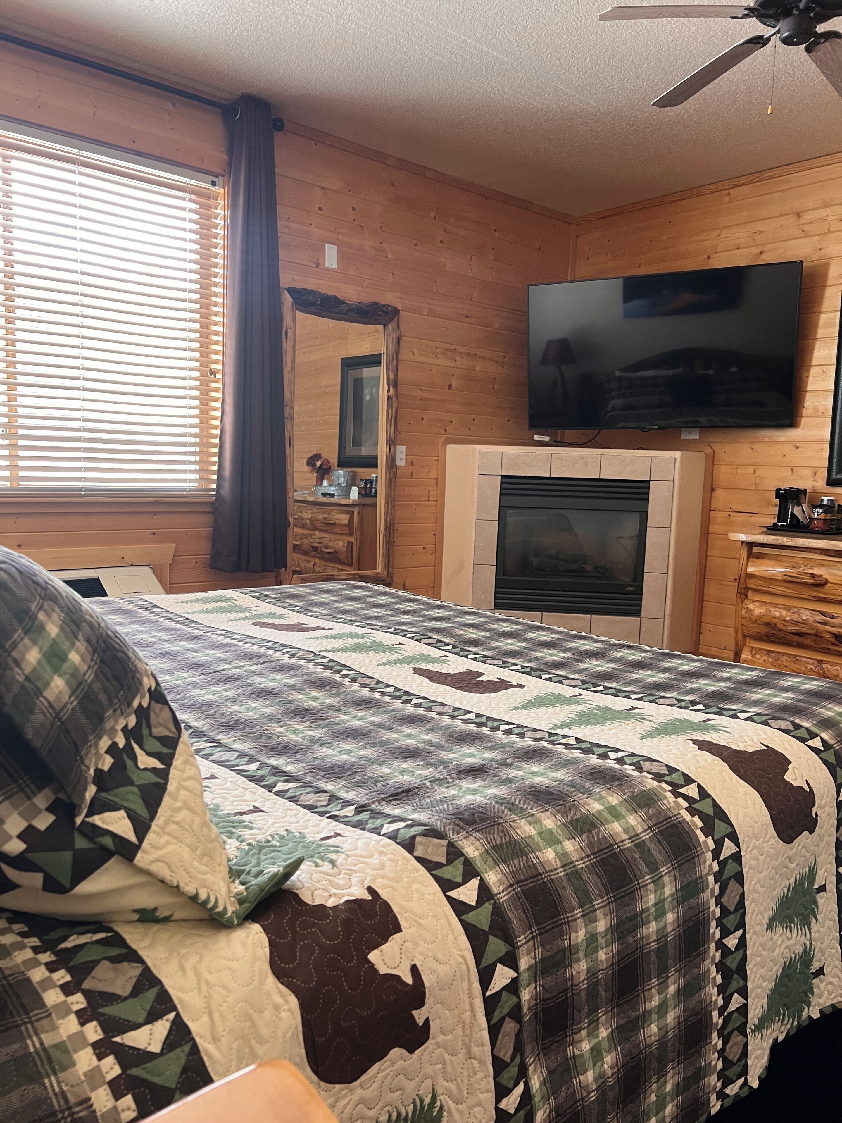 A cozy room with a bed, a fireplace, a TV, and a window with blinds.