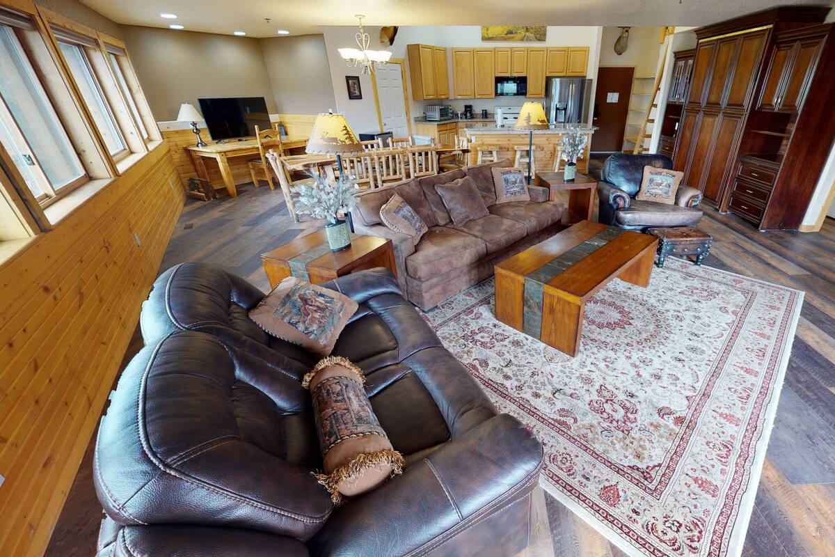 A spacious living room with a large leather sectional sofa, a wooden coffee table, and a patterned rug.