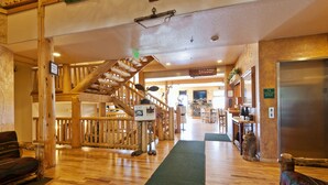 A hotel lobby with a wooden staircase, a reception desk, and a view of the dining area.