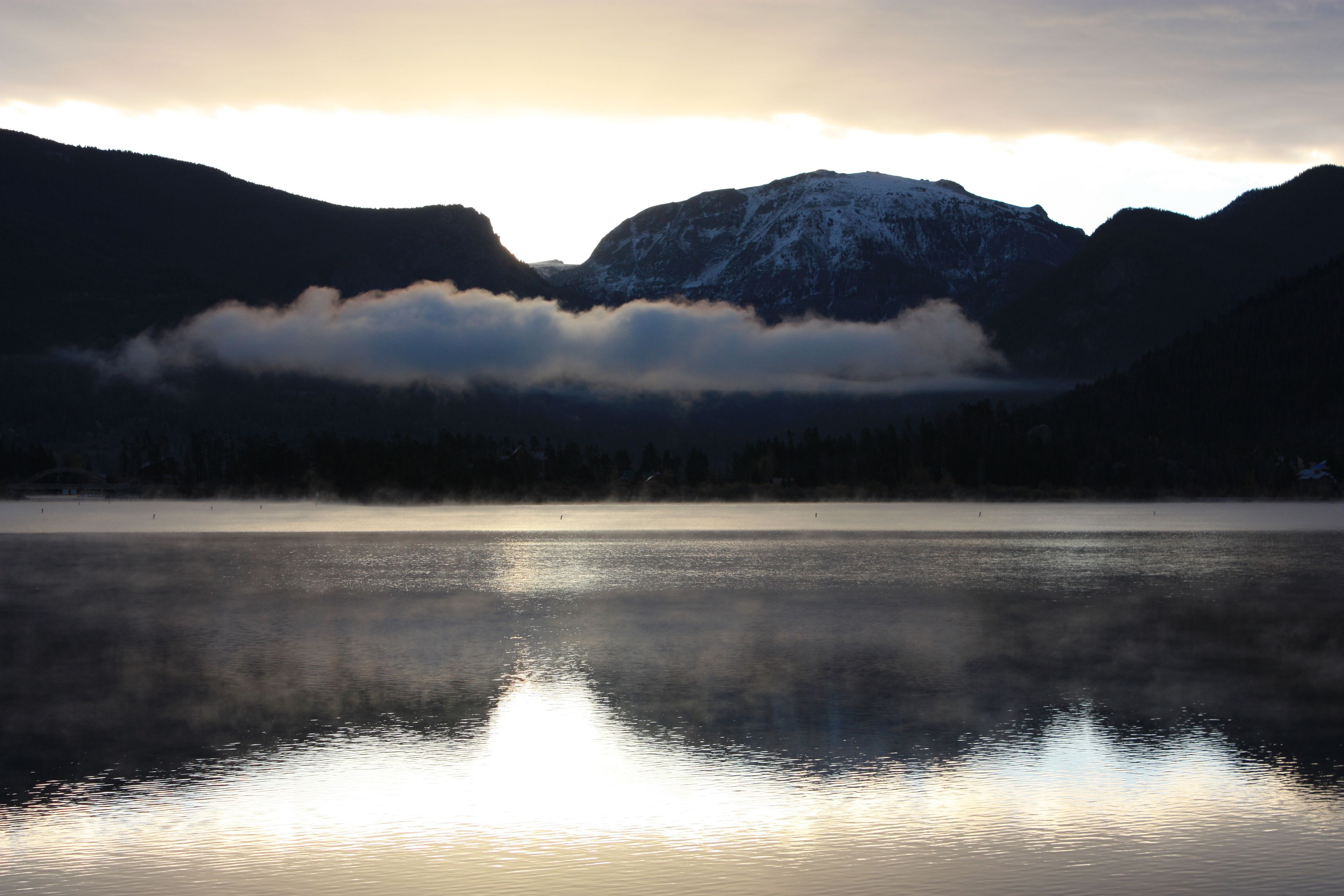 A calm lake with mountains in the background and a cloudy sky.