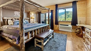 A rustic bedroom with a four-poster bed, a bench, a desk, and a view of the outdoors.
