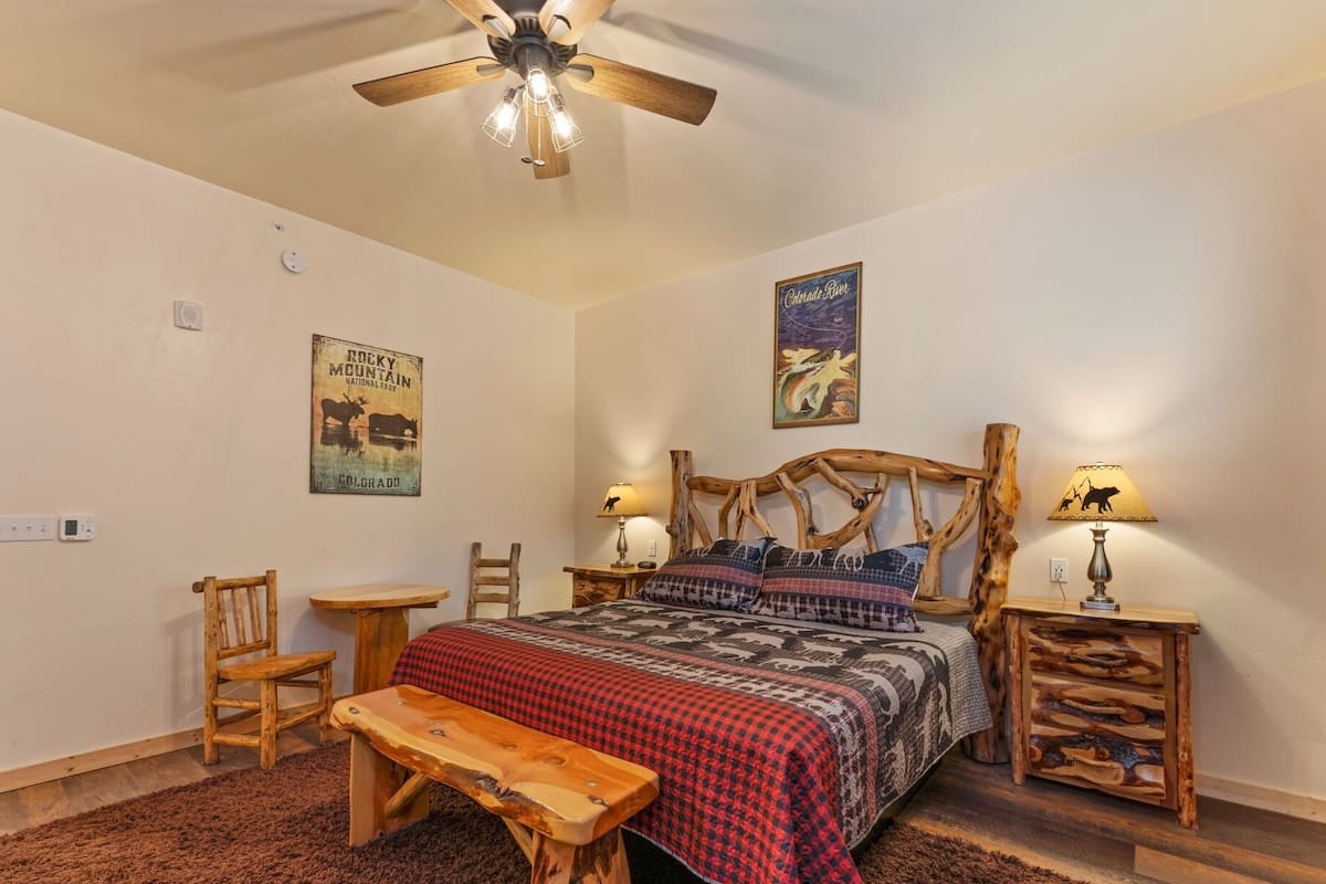 A bedroom with a wooden bed, a wooden bench, a ceiling fan, and two wall-mounted lamps.
