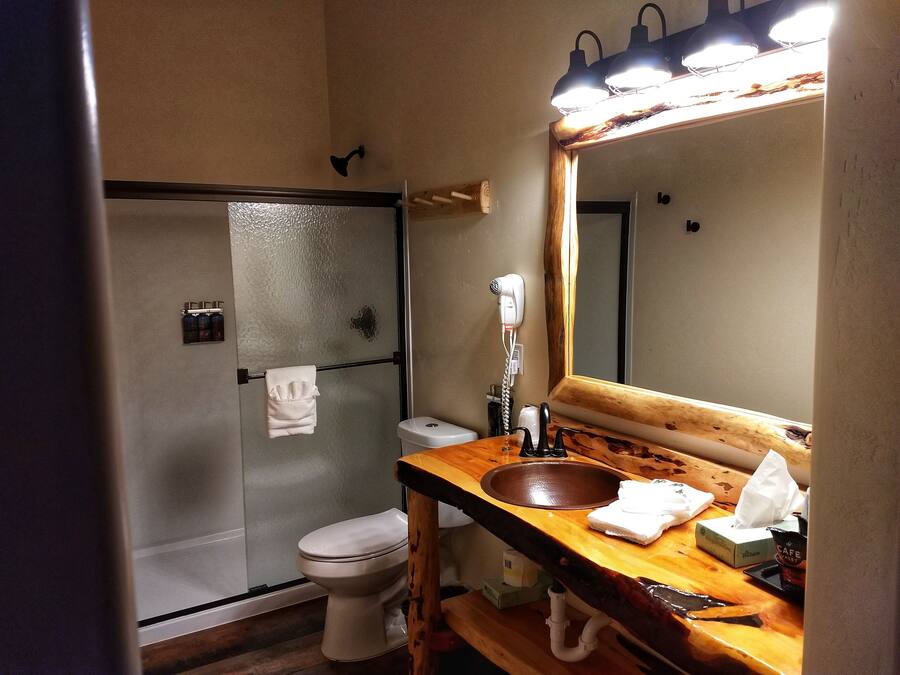 A bathroom with a wooden vanity, a glass shower enclosure, a toilet, and a mirror with lights.