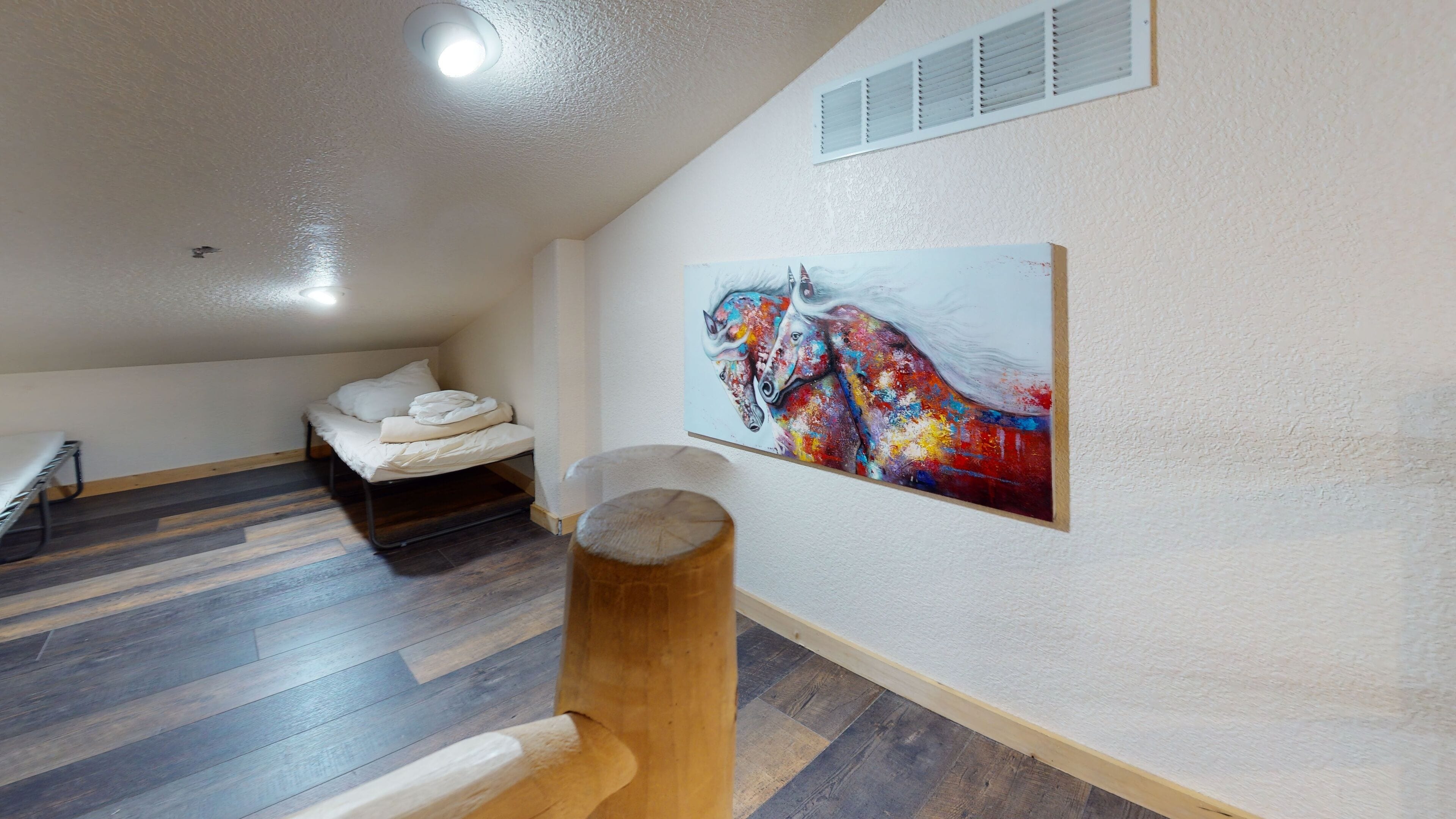 A small, cozy room with a bunk bed, a wooden stool, and a colorful painting on the wall.