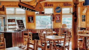 A rustic wooden interior with tables and chairs, a ceiling fan, and a mounted deer head.