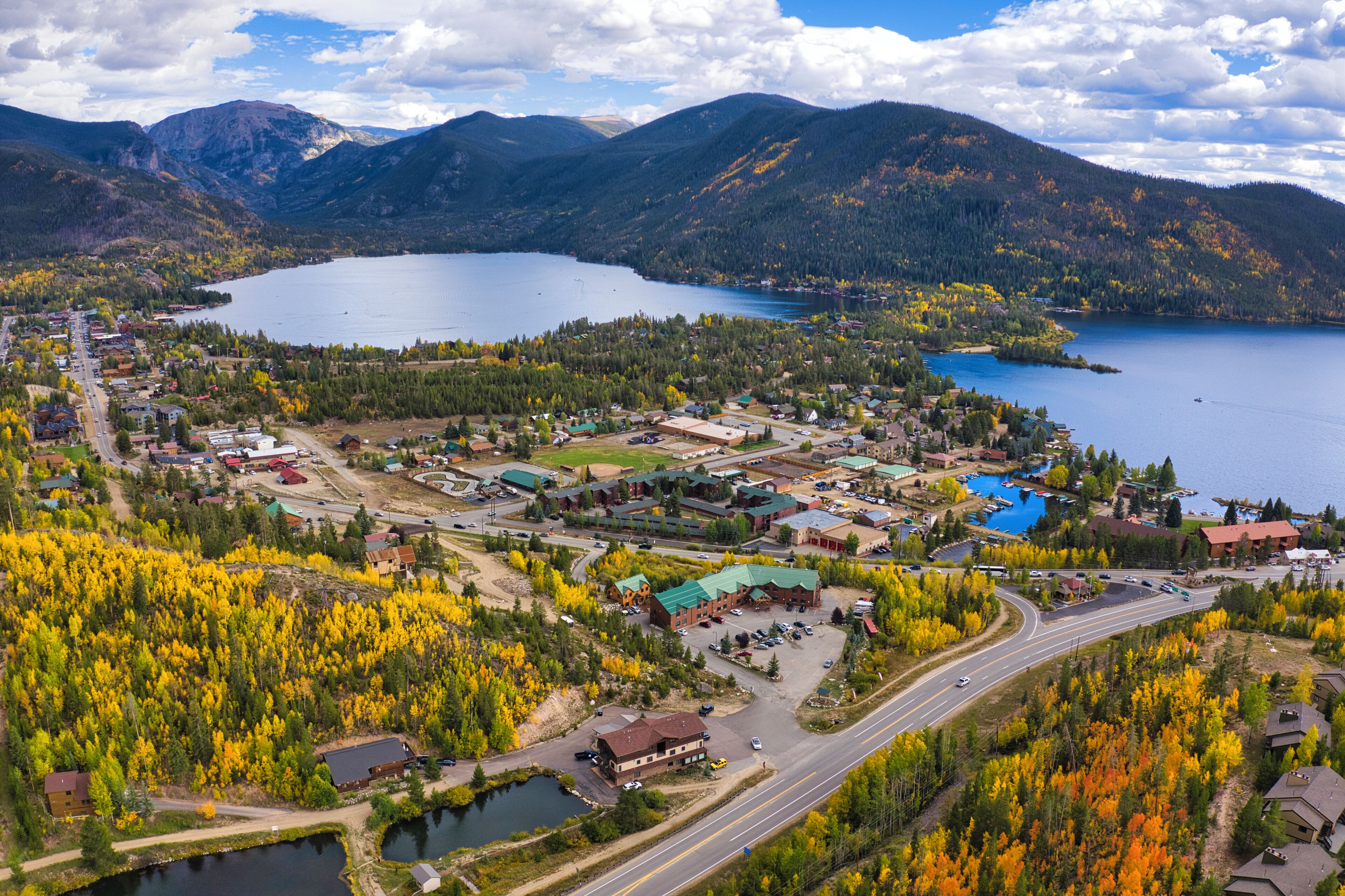 An aerial view of a lakeside town with buildings, roads, and a body of water surrounded by mountains.