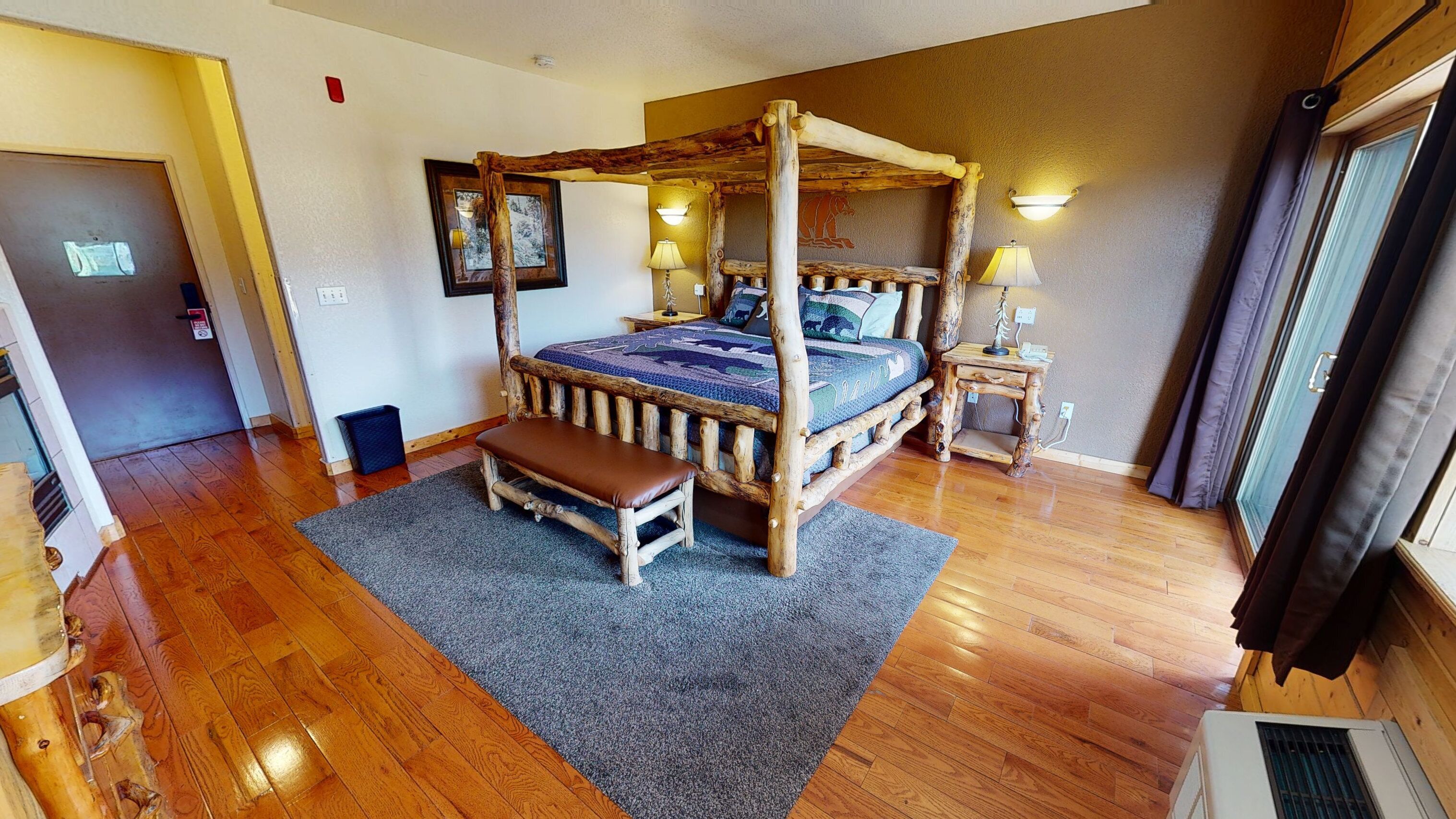 A four-poster bed with a bench, a small bedside table, and a wall-mounted lamp.