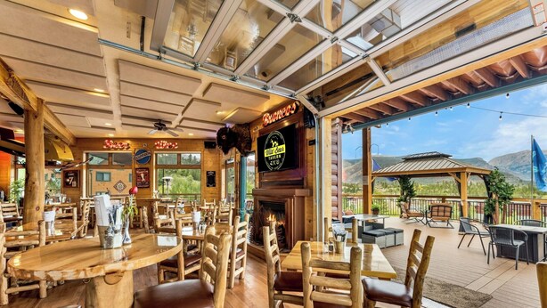 A restaurant with wooden interiors, a fireplace, and outdoor seating with a mountain view.