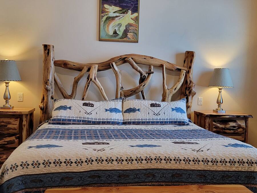 Ein Bett mit einem einzigartigen Holzkopfteil, zwei Nachttische mit Lampen, eine Bettdecke mit Fischmuster und ein Bild an der Wand.