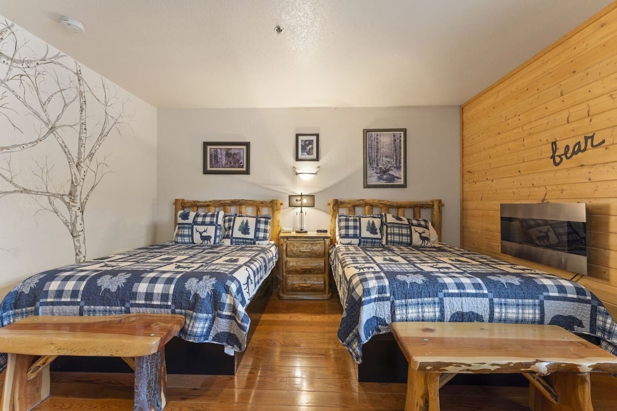 A room with two wooden beds, a small table, and a wall-mounted TV.