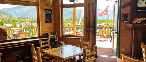 Interior de madera con una mesa, sillas, cabeza de venado montada y vistas a montañas a través de la puerta.