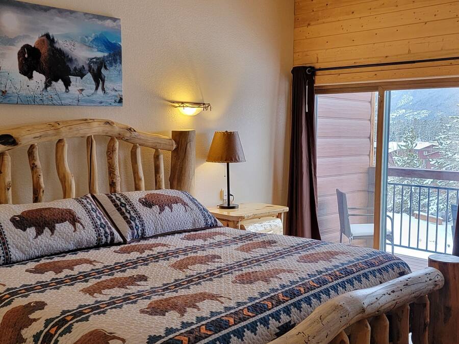 Ein Bett mit Holzrahmen, Bettwäsche mit Büffelmotiven, ein Bisonbild an der Wand und ein Blick ins Freie durch ein Fenster.