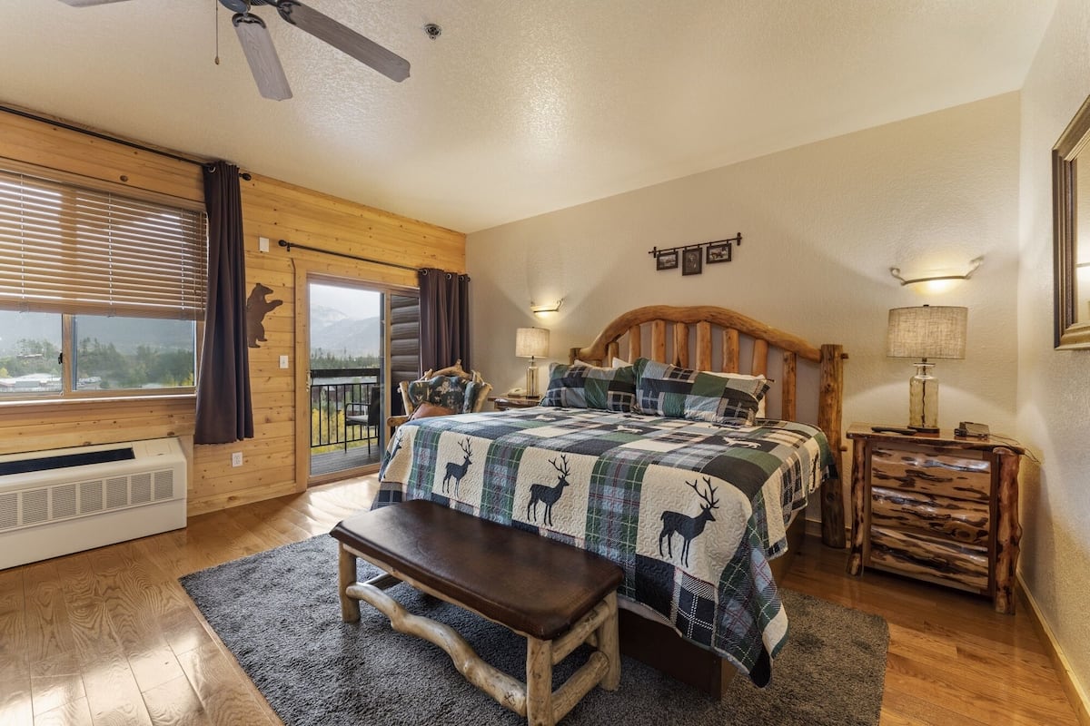 A cozy bedroom with a wooden bed, a bench, a nightstand, and a view of the outdoors through a sliding door.