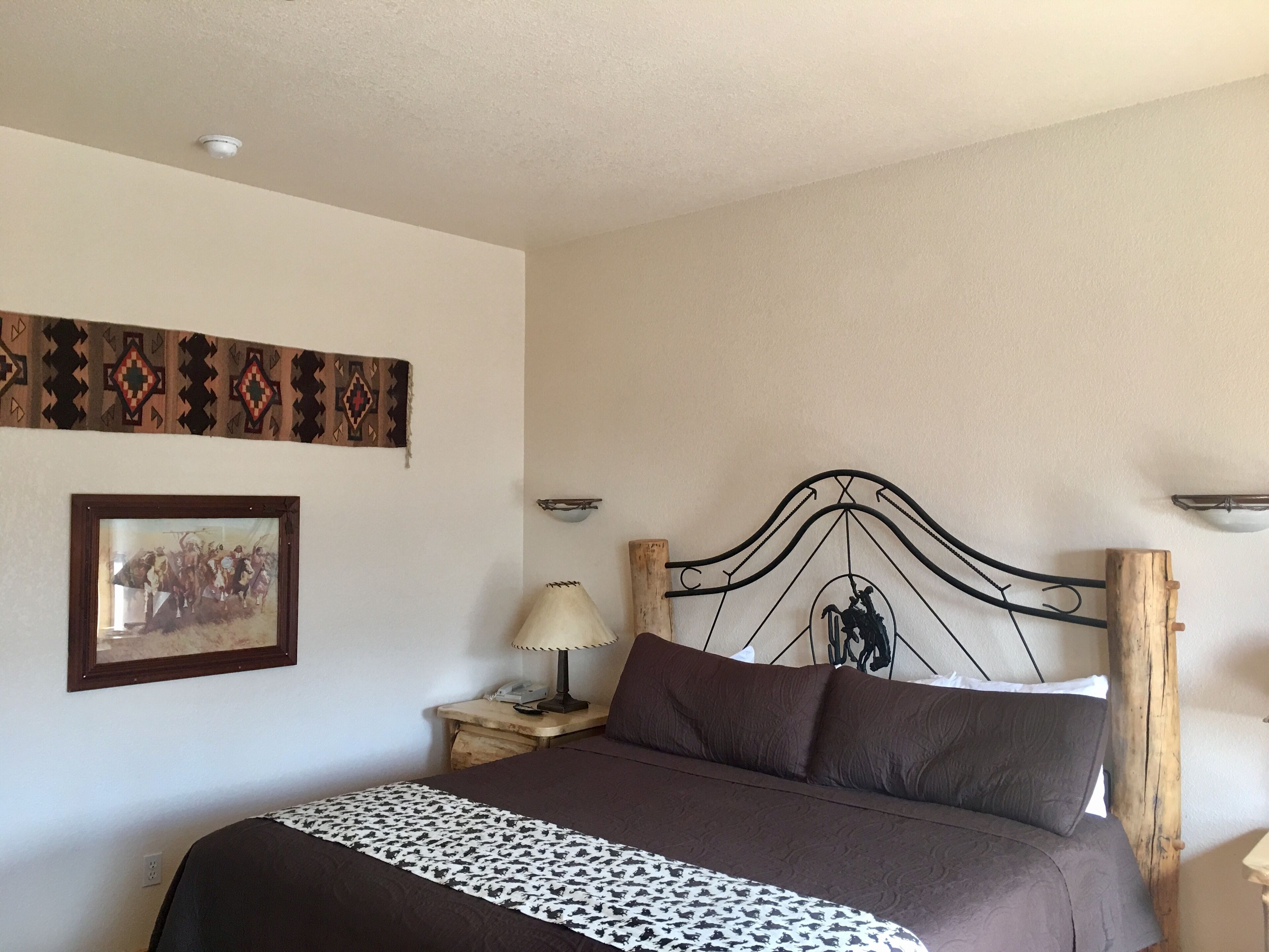 Un dormitorio con cama, mesita de noche, lámpara, un cuadro en la pared y un cabecero decorativo.