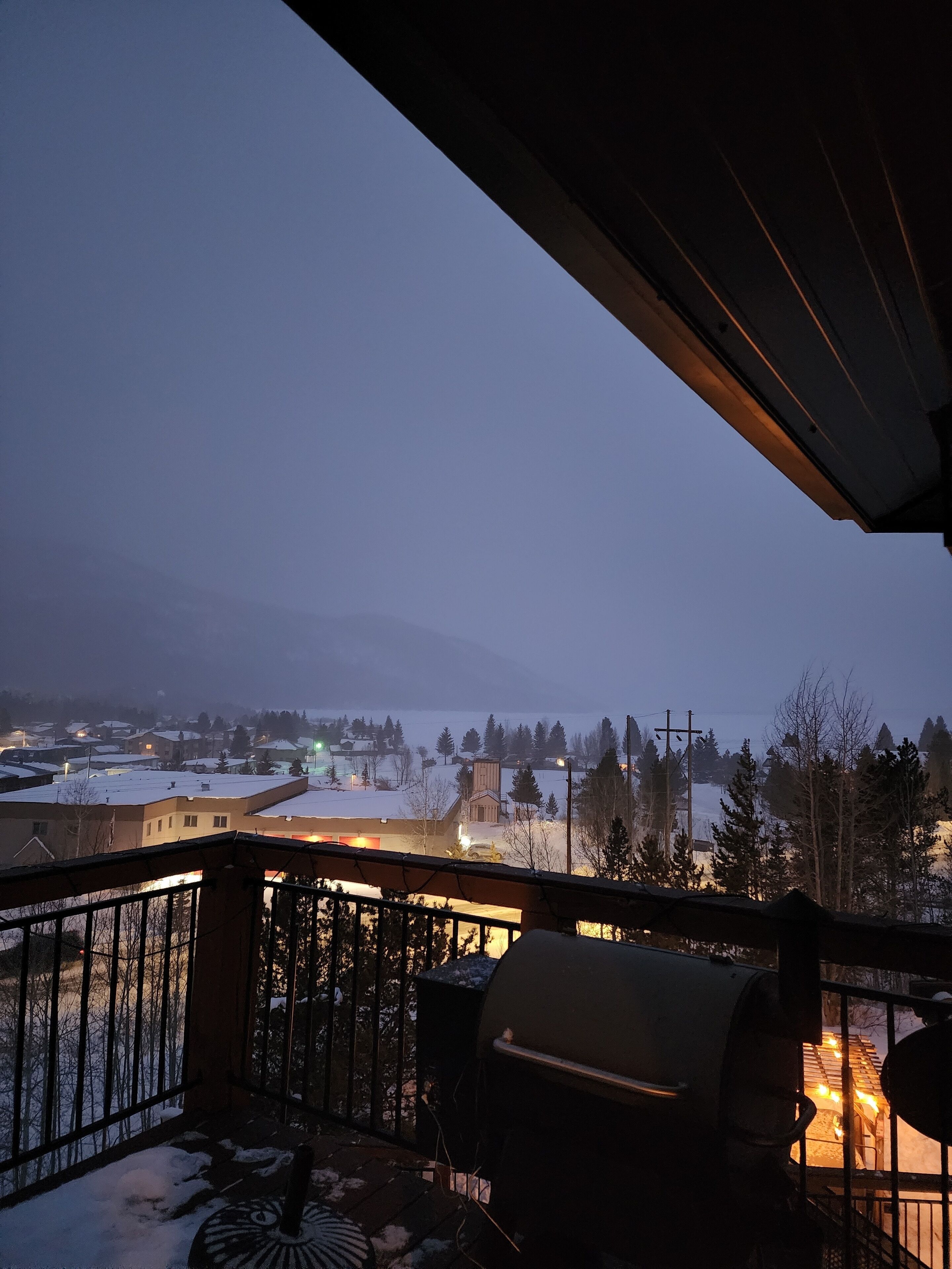 Ein Balkon mit Grill und Blick auf eine verschneite Landschaft sowie Gebäude in der Ferne.