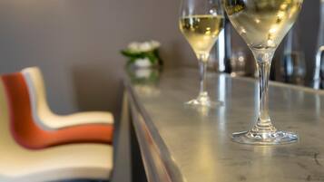 A bar area with two glasses of white wine on a counter, a modern chair design, and a wall-mounted light fixture.