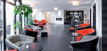 Un área de lounge moderna con diferentes disposiciones de asientos, incluyendo sofás y sillones, y una gran planta en maceta.