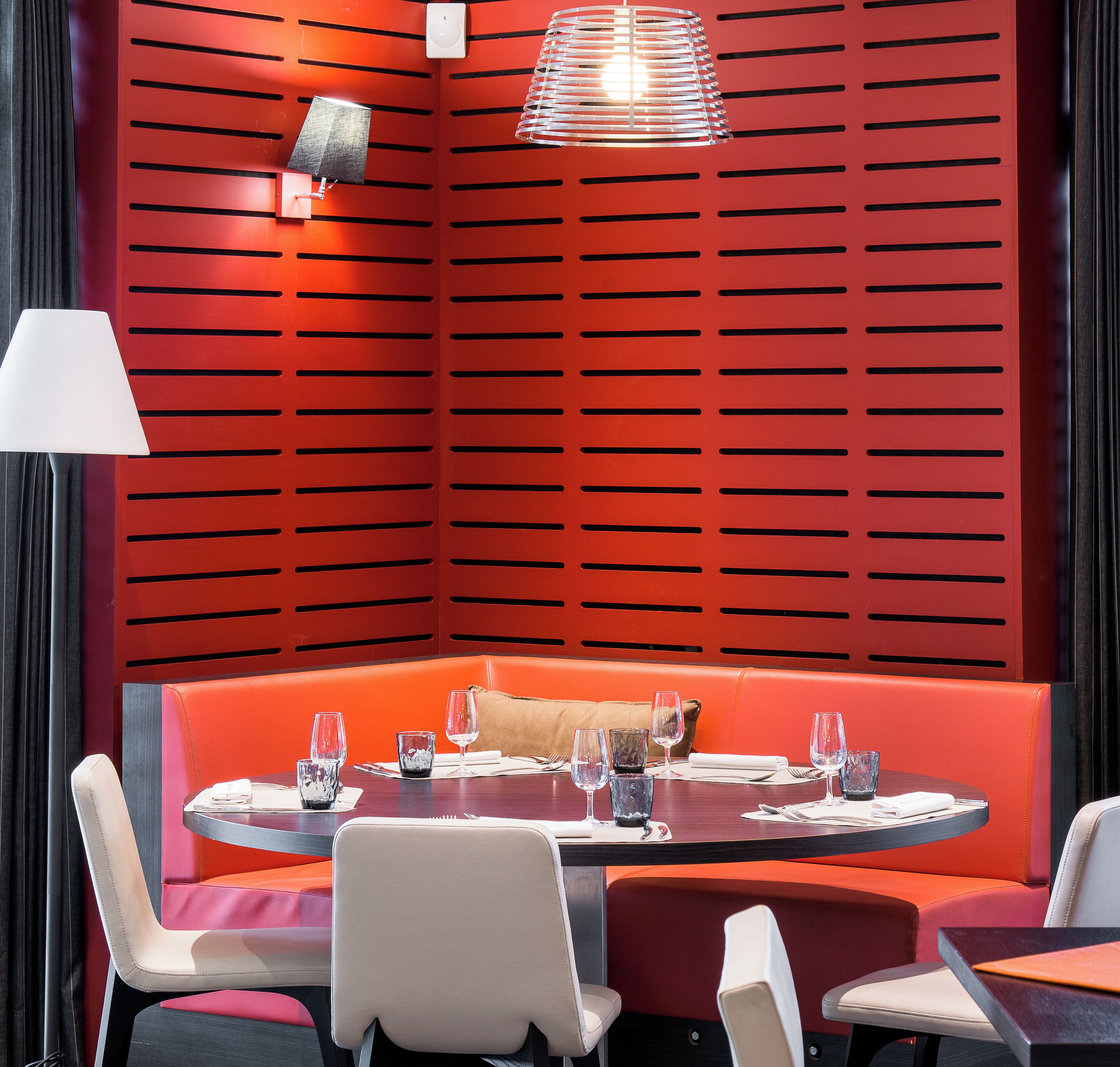 A dining area with a red wall, a round table, and cushioned seating.