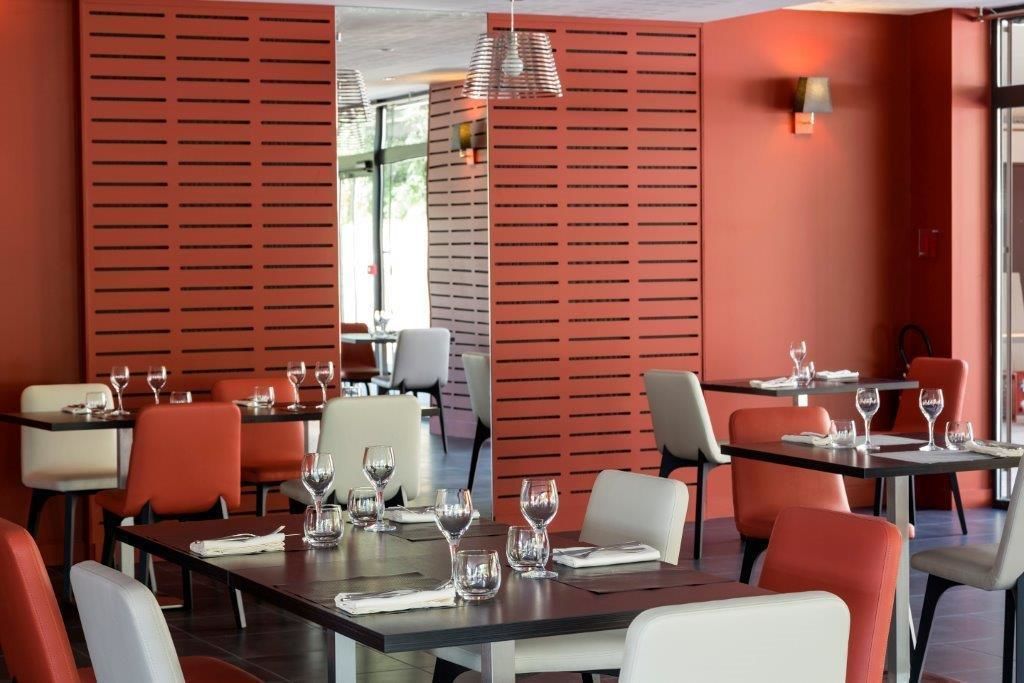Un restaurant à la décoration rouge et blanche, avec des tables dressées, ornées de verres à vin et d’assiettes, et un aménagement intérieur moderne.