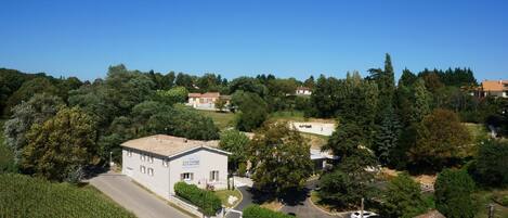 Un pueblo rural con un edificio blanco identificado como "La Cogne" en primer plano, rodeado de exuberante vegetación y un cielo azul despejado.