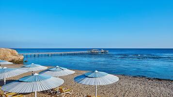 A beach with umbrellas and lounge chairs, a pier extending into the sea, and clear skies.