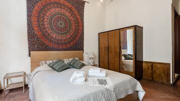 Una cama bien hecha con colcha blanca, cabecera de madera y un tapiz con diseño circular en la pared.