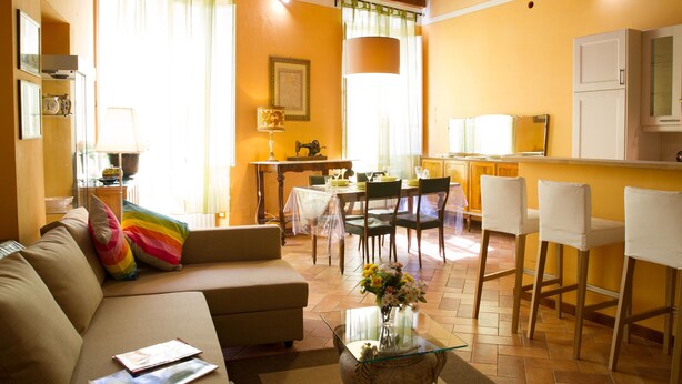 A living room with a sofa, a glass coffee table, and a dining area with chairs and a table. - La Gemma di Elena (Lucca)