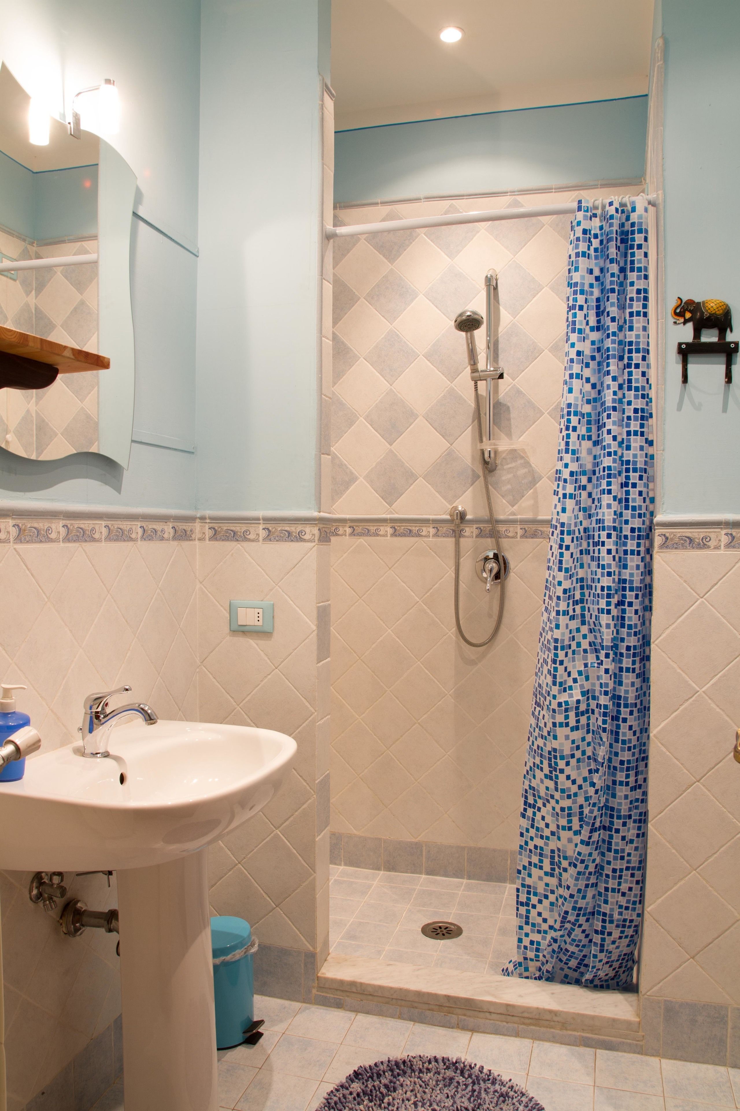 Un baño con ducha, lavamanos y cortina de baño azul estampada.