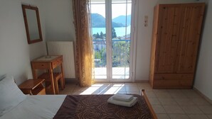 Une chambre à coucher comprenant un lit, une armoire en bois, un bureau et une vue sur un lac, visible à travers une porte vitrée.