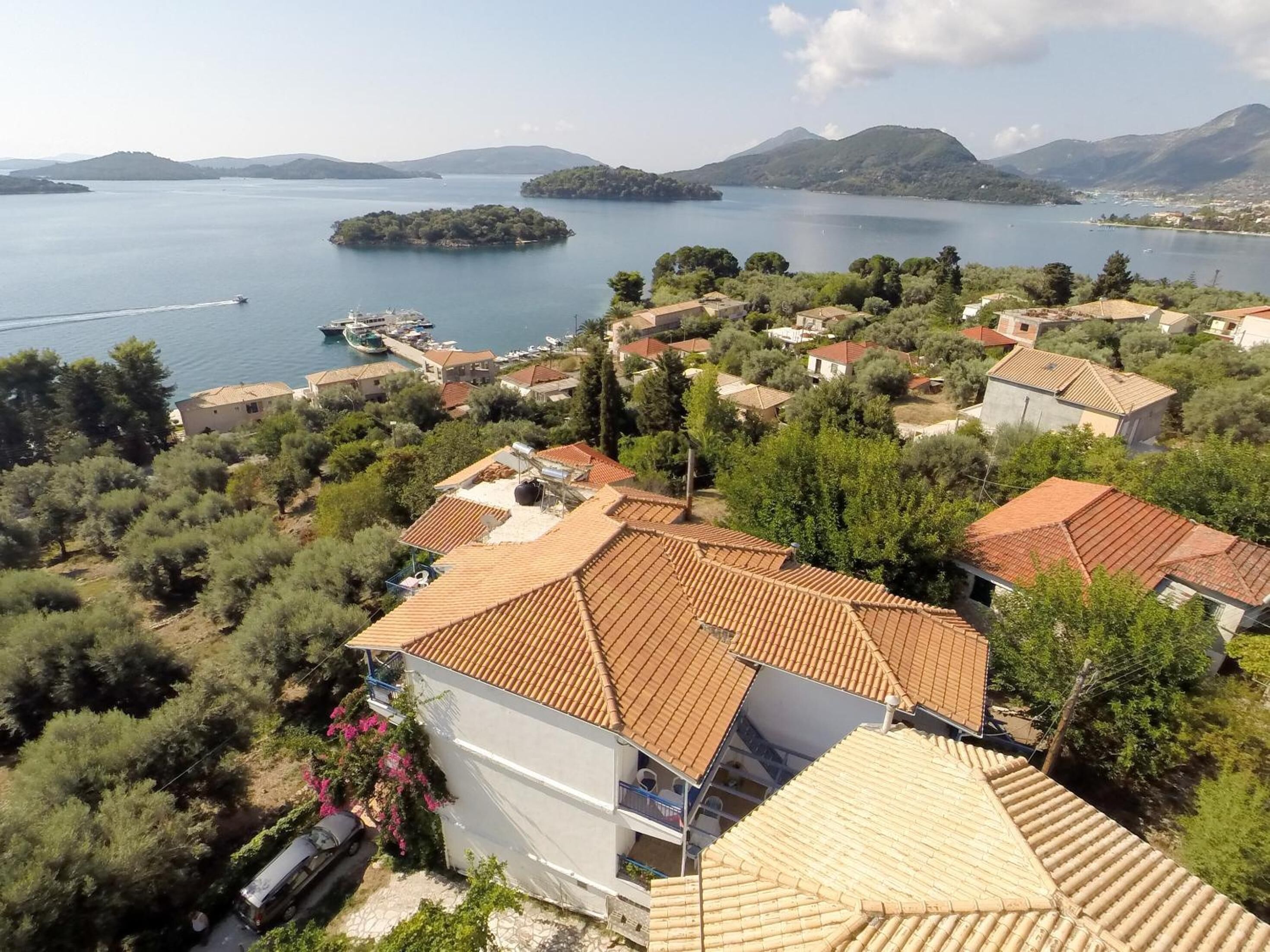 A coastal village with terracotta-roofed houses, a marina, and a view of the sea and islands.
